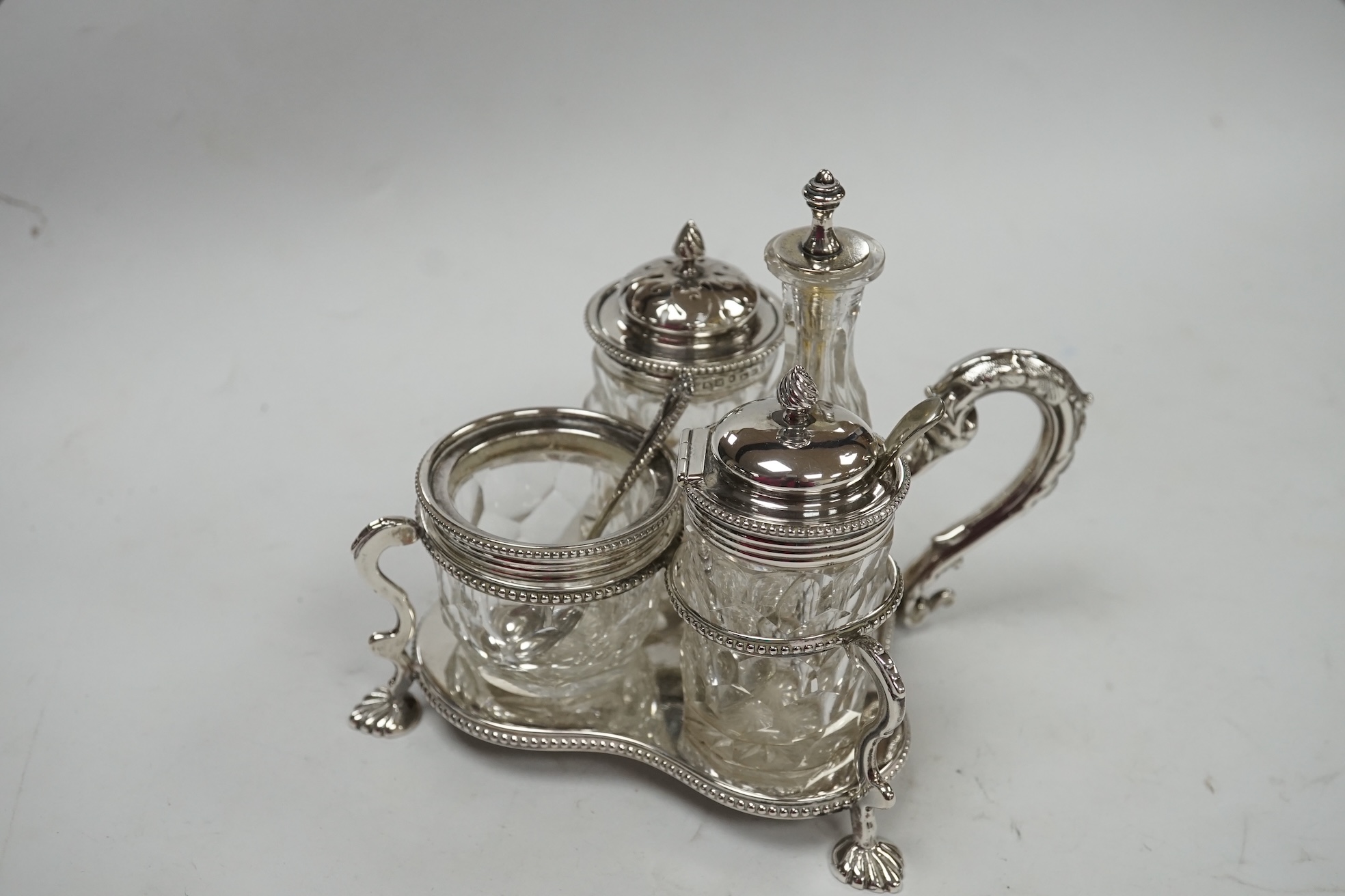 A late Victorian silver cruet stand, Jane Brownett, London, 1879, with four silver mounted bottles, different maker, Birmingham, 1879, height 67mm, together with a later silver mustard pot, a George V silver mounted phot